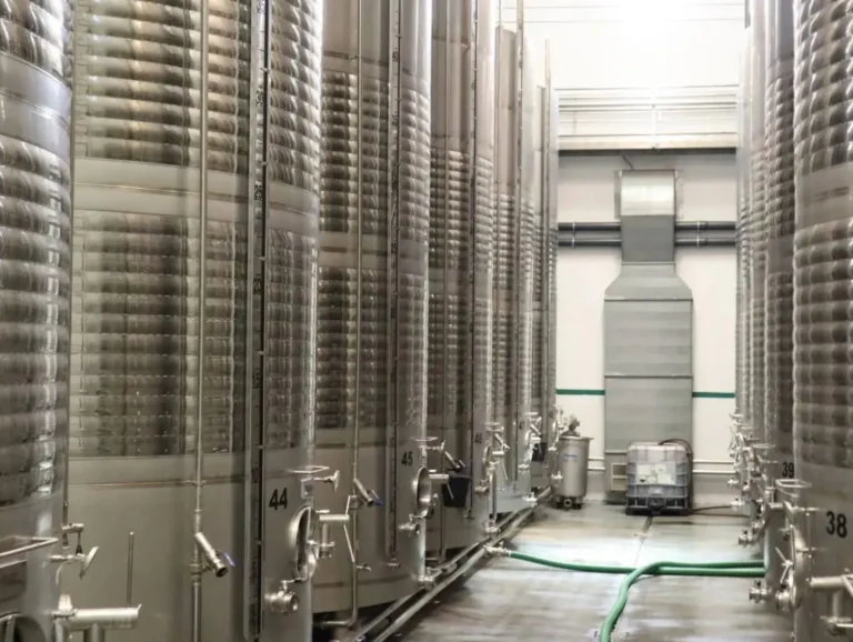 Interior de una bodega con grandes depósitos cilíndricos de acero inoxidable numerados, utilizados para la producción de vino y mosto en Castilla-La Mancha, sector beneficiario de las ayudas APPaas.