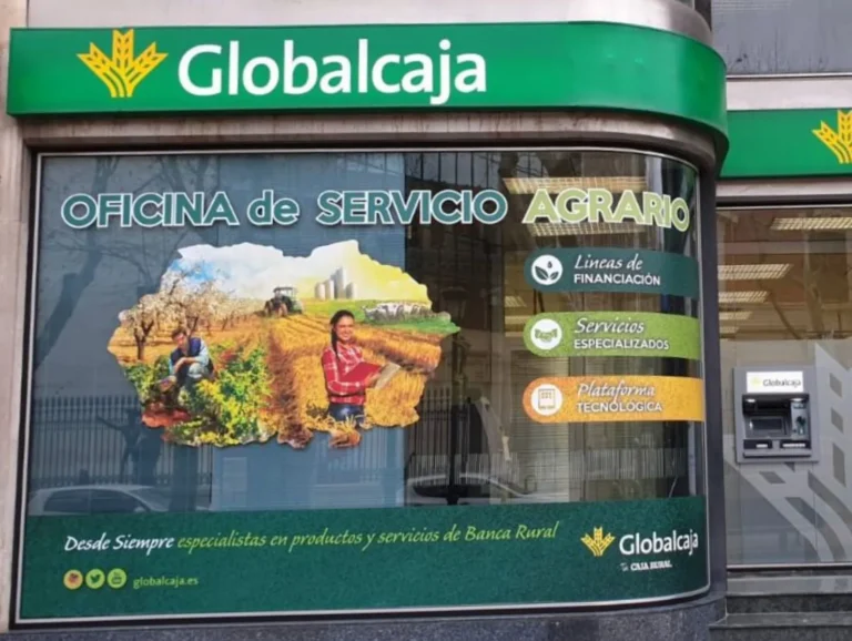 Fachada de una oficina de Globalcaja con cartelería de "Oficina de Servicio Agrario" y mensajes sobre la gestión de la PAC, entidad colaboradora en Castilla-La Mancha.