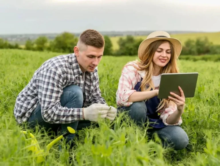Dos agricultores, un hombre y una mujer, colaborando en un campo verde con una tablet, beneficiarios de las ayudas de titularidad compartida.